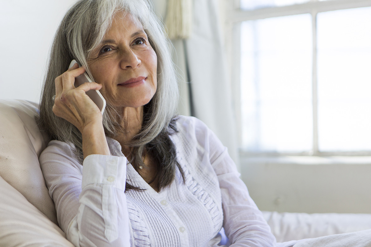 A women sitting on her couch making a phone call with her smart phone at her ear