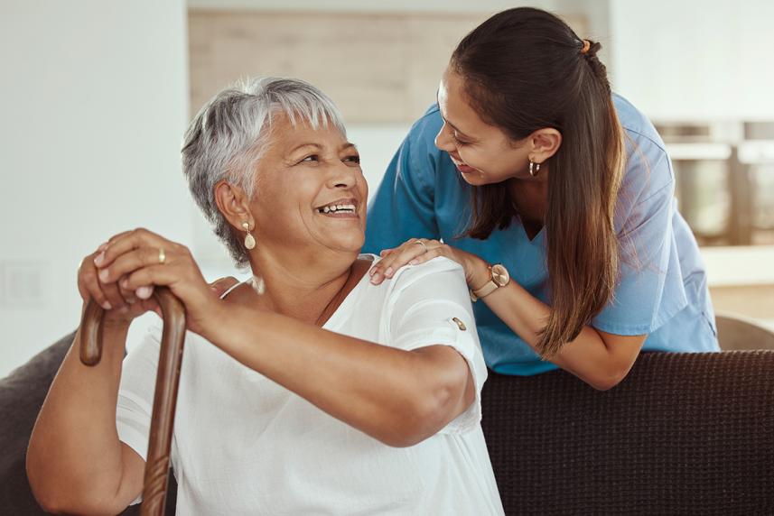 A home health aide helps an elder with a cane