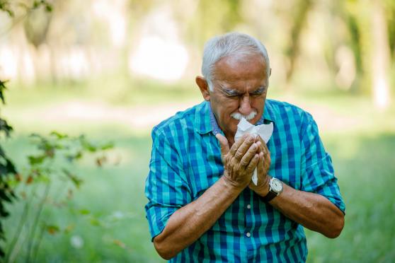 Senior man sneezing in a tissue outside