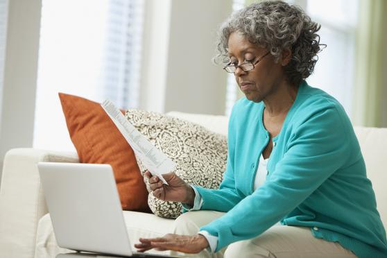 An elder sits on a couch and uses a laptop