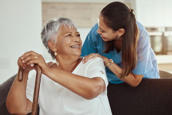 A home health aide helps an elder with a cane