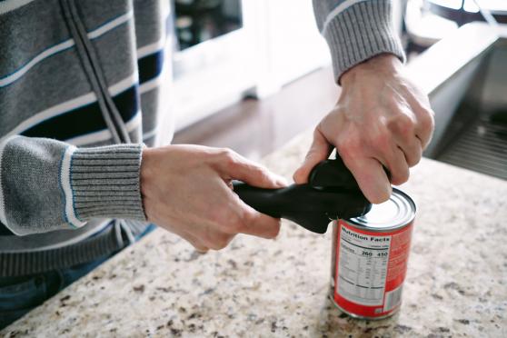 Hands use a can opener to open a can