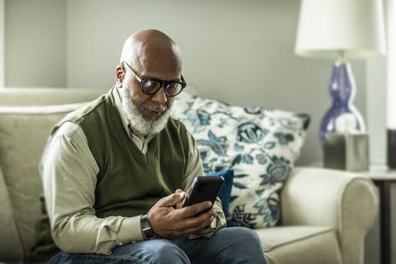 An elder sits on a couch and looks at a mobile phone