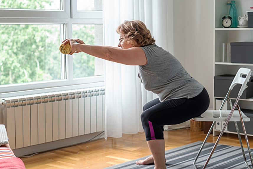 A woman squatting over a chair and holding a rolled up towel.