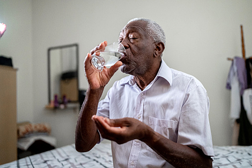A man holding a pill and drinking from a glass of water