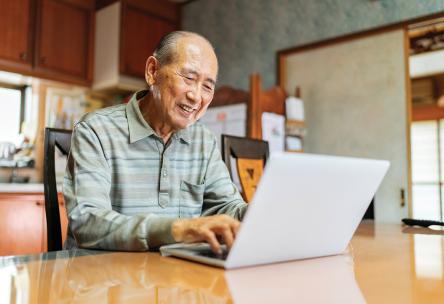 A senior man works on a laptop in his kitchen