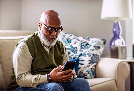 An elder person sits on a couch and uses a smartphone