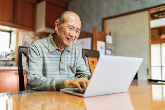 A senior man works on a laptop in his kitchen