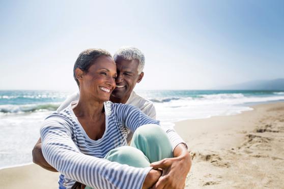 An older black couple sitting on the beach