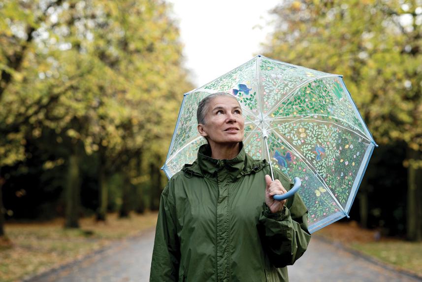 older woman walking outside in rain with umbrella